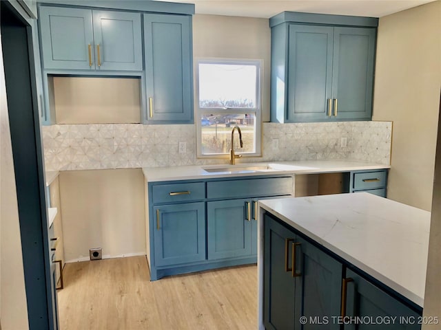 kitchen with light wood finished floors, tasteful backsplash, blue cabinetry, and a sink