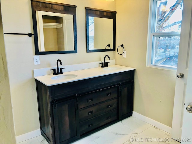 full bathroom featuring marble finish floor, double vanity, a sink, and baseboards