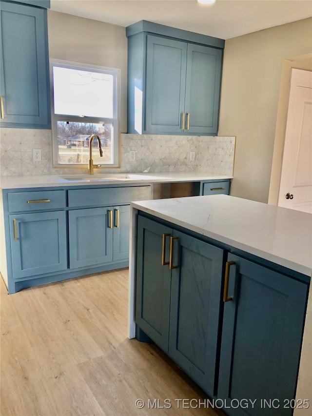 kitchen with light wood finished floors, blue cabinetry, backsplash, and a sink