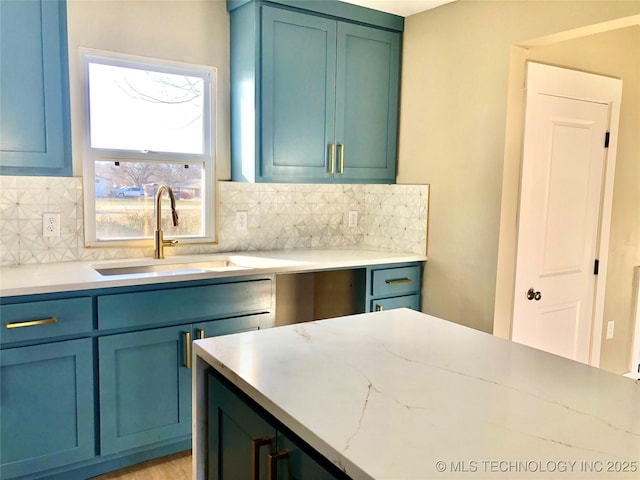 kitchen with light stone counters, backsplash, a sink, and blue cabinets