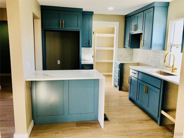 kitchen featuring a peninsula, a sink, light countertops, light wood-type flooring, and backsplash