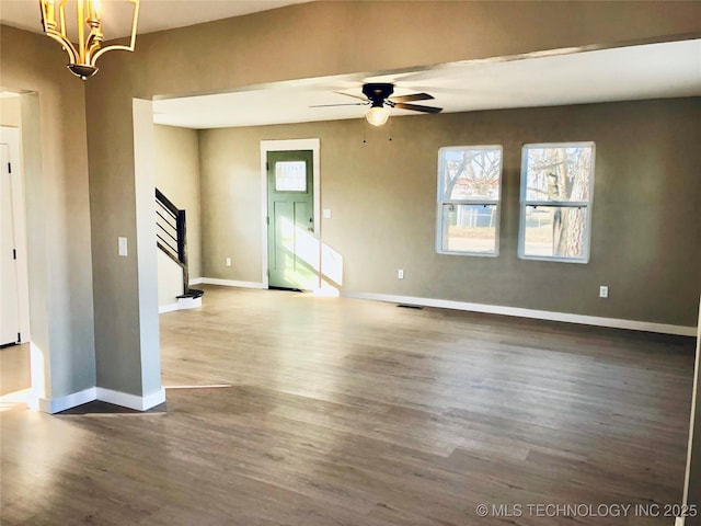 empty room featuring visible vents, baseboards, a ceiling fan, dark wood-type flooring, and stairs