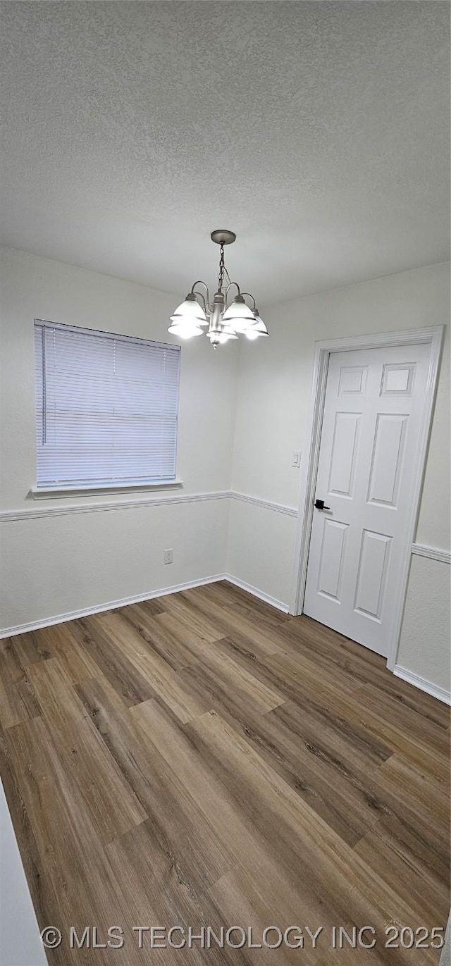 unfurnished dining area featuring hardwood / wood-style flooring, a textured ceiling, and a chandelier