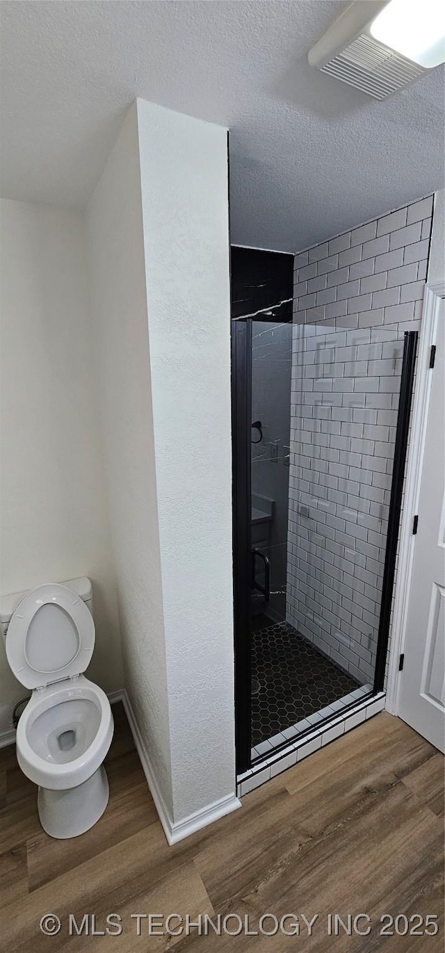 bathroom featuring toilet, a textured ceiling, hardwood / wood-style floors, and a shower with door