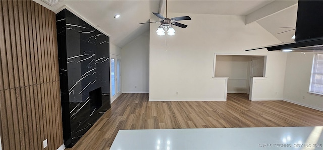 unfurnished living room featuring hardwood / wood-style flooring, a premium fireplace, vaulted ceiling with beams, and ceiling fan