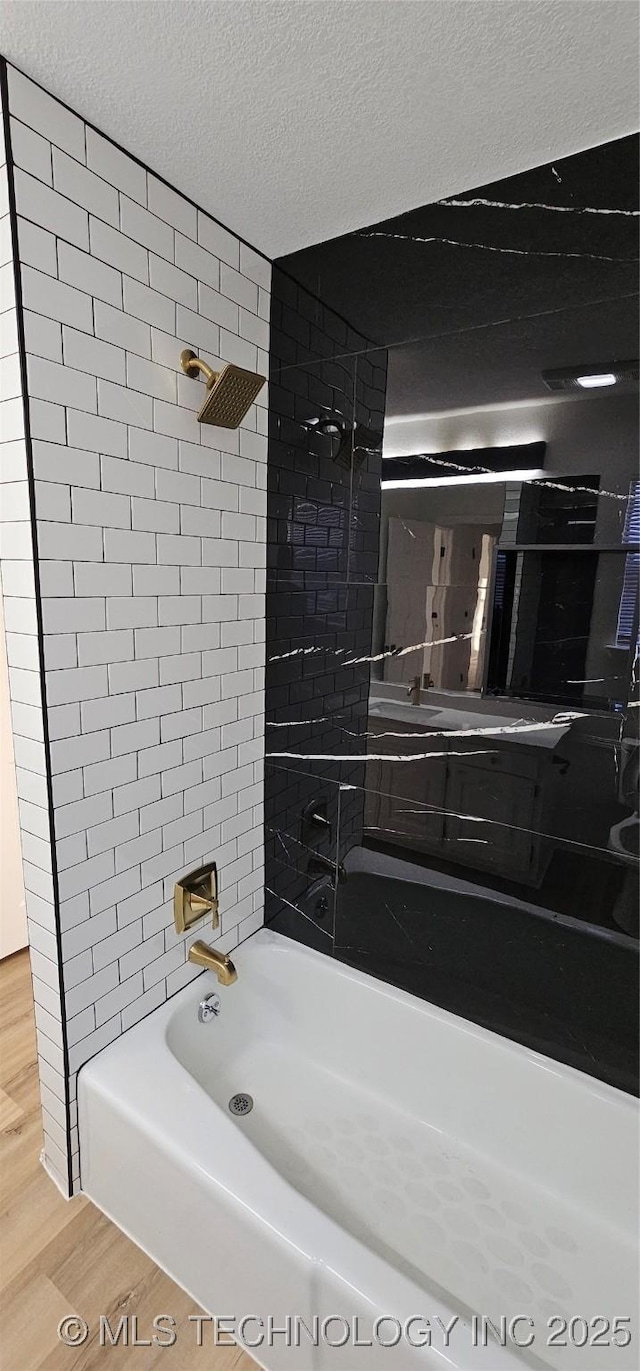 bathroom with a textured ceiling, tiled shower / bath, and wood-type flooring