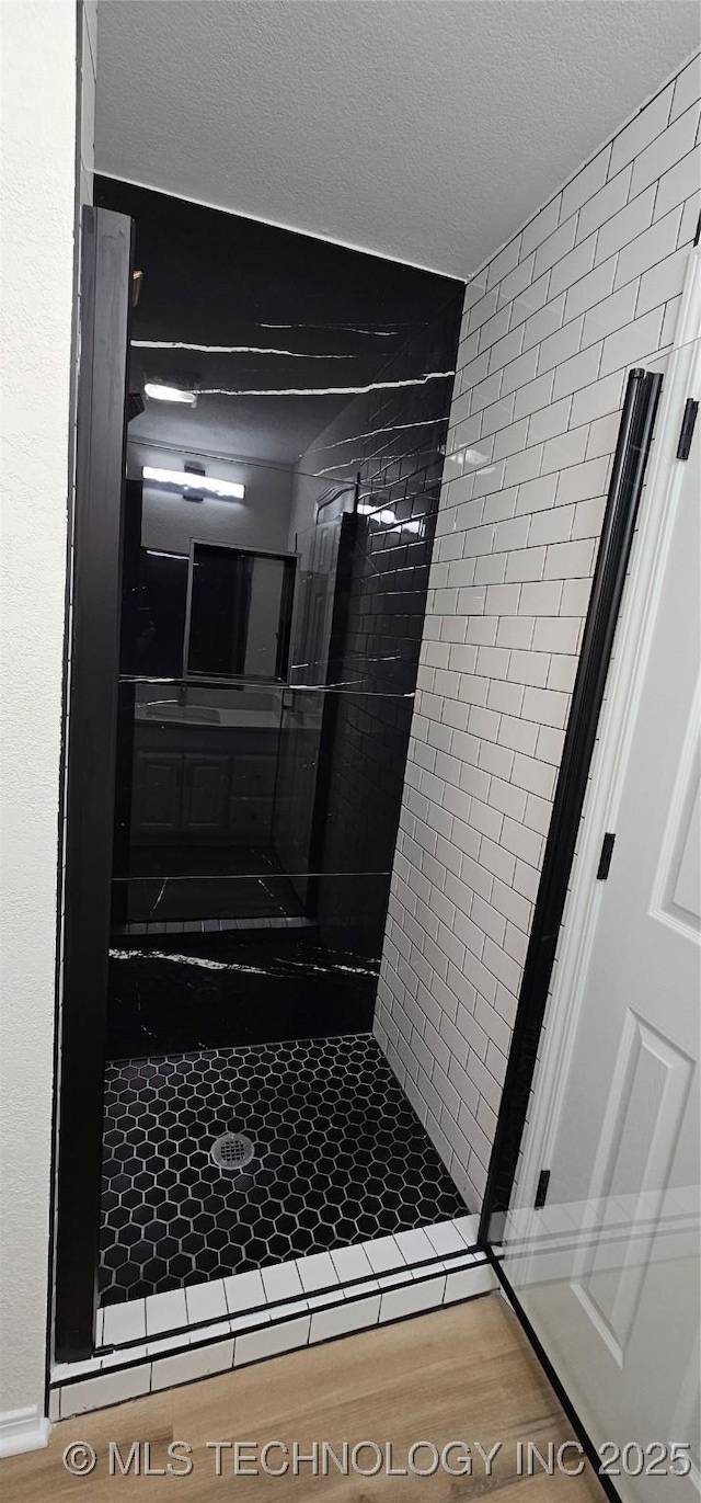 bathroom featuring wood-type flooring, a tile shower, and a textured ceiling