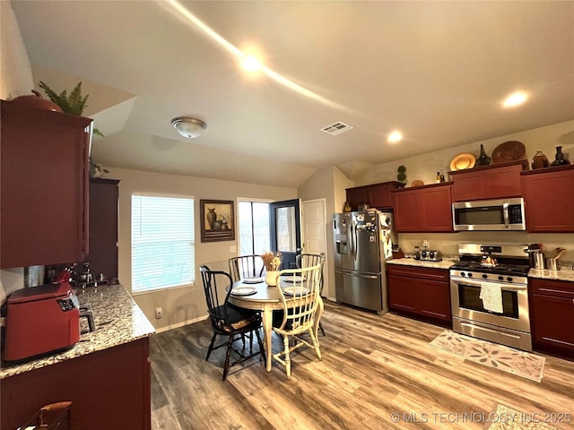 kitchen with light stone counters, appliances with stainless steel finishes, lofted ceiling, and light wood-type flooring