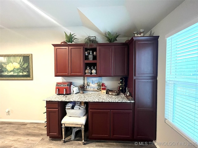 bar featuring vaulted ceiling, light stone counters, and light hardwood / wood-style floors