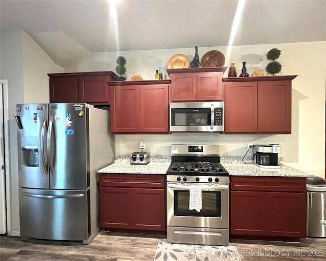 kitchen with light stone countertops, wood-type flooring, and appliances with stainless steel finishes