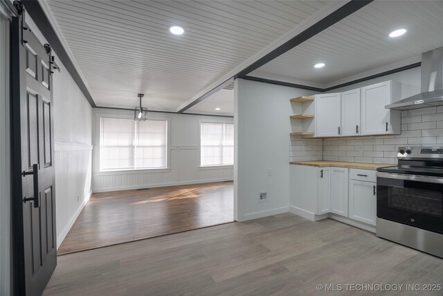 kitchen featuring stainless steel electric stove, a barn door, butcher block counters, and white cabinets