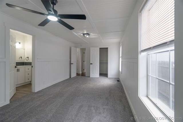 unfurnished bedroom with multiple windows, ensuite bathroom, light colored carpet, and ceiling fan