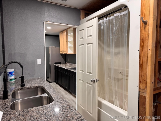 kitchen with sink, dark stone countertops, and stainless steel refrigerator