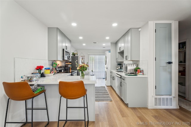 kitchen featuring stainless steel appliances, light hardwood / wood-style floors, kitchen peninsula, and tasteful backsplash