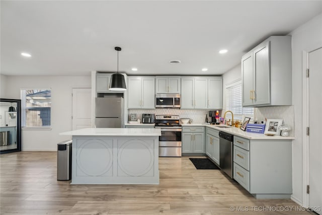 kitchen featuring decorative light fixtures, gray cabinets, a kitchen island, sink, and appliances with stainless steel finishes