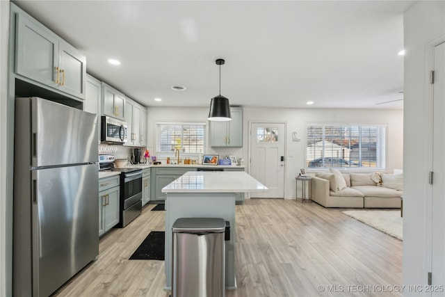 kitchen featuring stainless steel appliances, backsplash, hanging light fixtures, light hardwood / wood-style flooring, and a center island