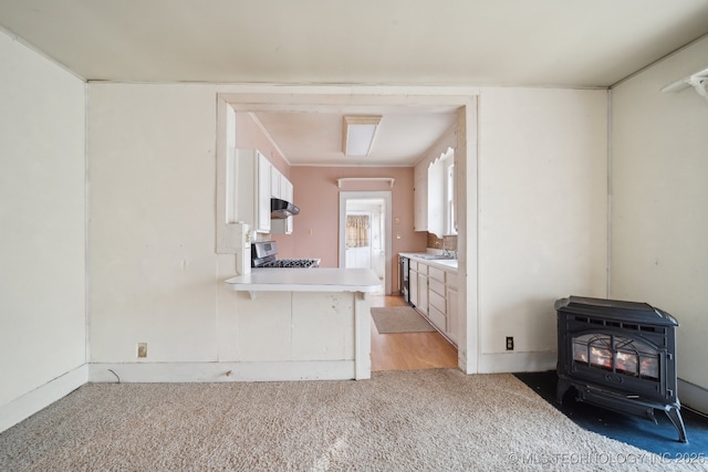 kitchen with kitchen peninsula, stainless steel range with gas stovetop, a wood stove, light colored carpet, and white cabinets