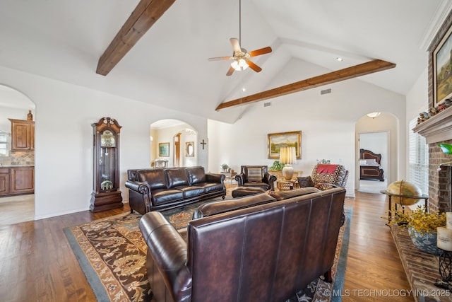 living room featuring ceiling fan, dark wood-type flooring, a fireplace, high vaulted ceiling, and beam ceiling