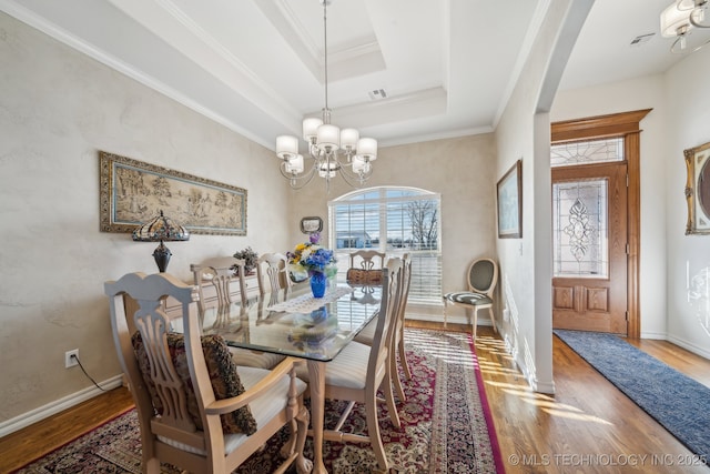 dining space with a raised ceiling, a chandelier, wood-type flooring, and ornamental molding