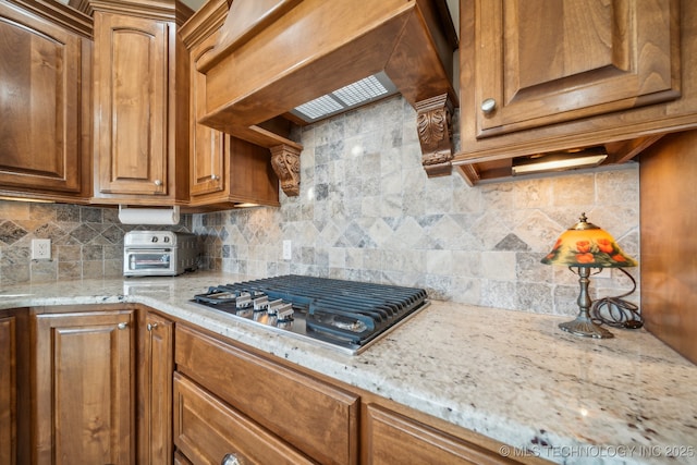 kitchen featuring stainless steel gas cooktop, custom exhaust hood, backsplash, and light stone counters