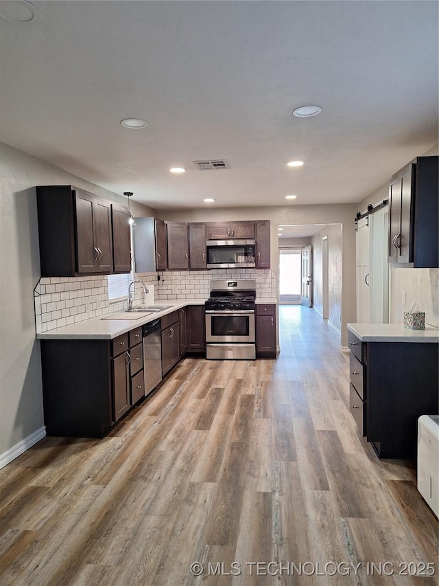 kitchen featuring dark brown cabinets, stainless steel appliances, light hardwood / wood-style floors, decorative light fixtures, and a barn door