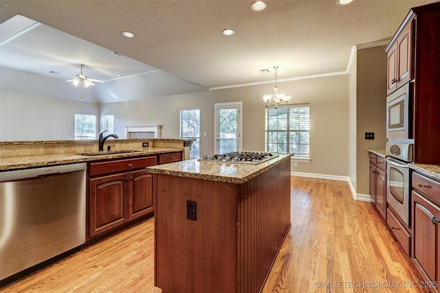 kitchen with decorative light fixtures, a center island, sink, light wood-type flooring, and appliances with stainless steel finishes