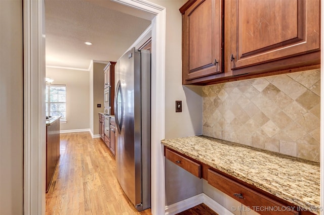 kitchen featuring light stone countertops, built in desk, stainless steel appliances, tasteful backsplash, and ornamental molding