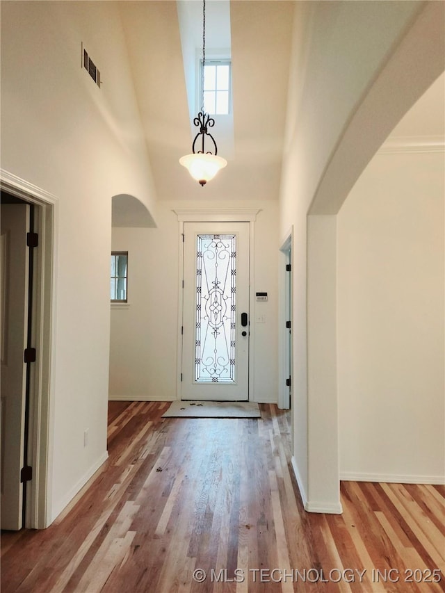 entryway featuring arched walkways, a high ceiling, light wood-style flooring, and visible vents