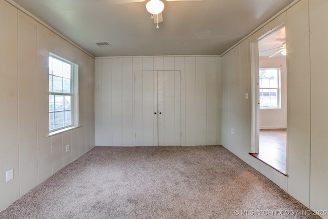 unfurnished bedroom with ceiling fan, wood walls, and carpet floors