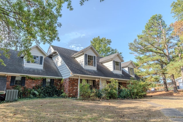 new england style home with brick siding, a front lawn, central AC, and roof with shingles