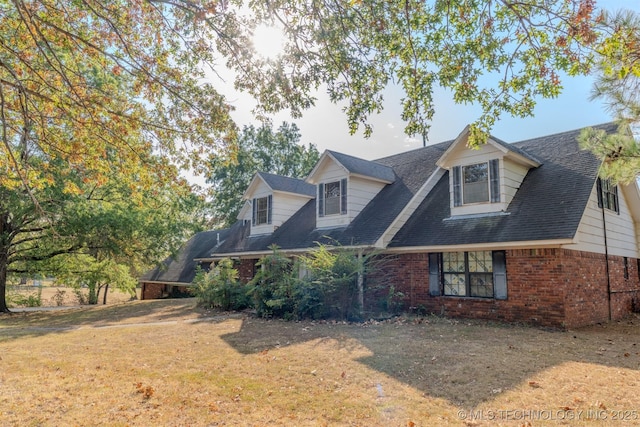 view of front facade featuring brick siding, a shingled roof, and a front yard