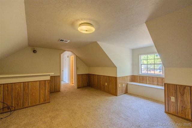 bonus room with wooden walls, visible vents, a wainscoted wall, vaulted ceiling, and a textured ceiling