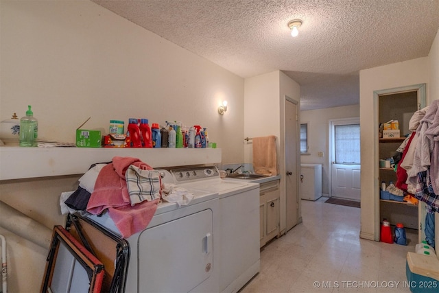 laundry room featuring washer and clothes dryer, light floors, cabinet space, a textured ceiling, and a sink