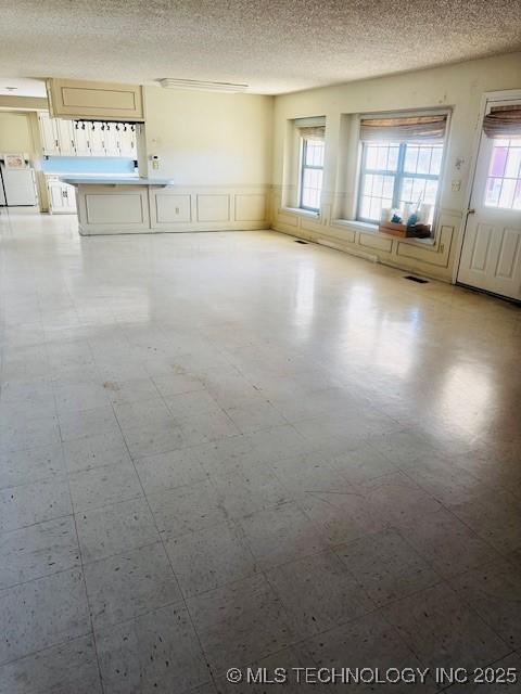 empty room with visible vents, a wainscoted wall, washing machine and clothes dryer, a textured ceiling, and tile patterned floors