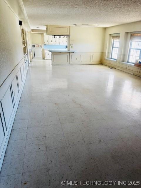 unfurnished living room with tile patterned floors, wainscoting, and a textured ceiling