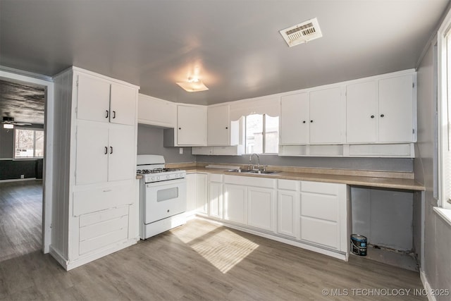 kitchen with hardwood / wood-style flooring, white cabinets, white gas stove, and sink