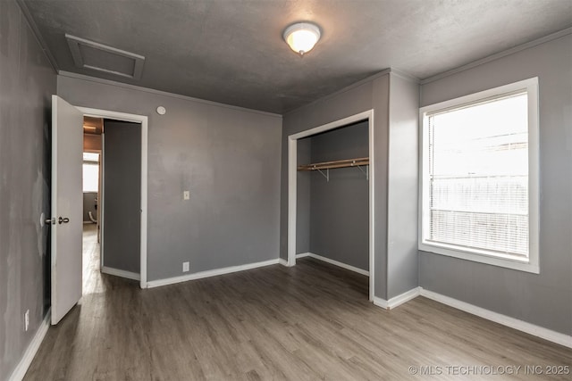 unfurnished bedroom with wood-type flooring, multiple windows, a closet, and crown molding