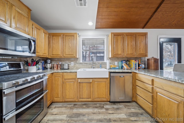 kitchen with tasteful backsplash, sink, light wood-type flooring, light stone countertops, and stainless steel appliances