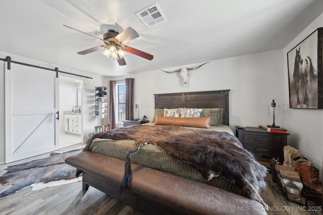 bedroom featuring ensuite bathroom, a barn door, ceiling fan, and hardwood / wood-style flooring