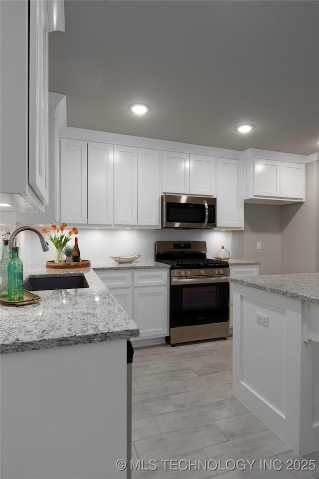 kitchen featuring light stone countertops, white cabinetry, stainless steel appliances, light hardwood / wood-style floors, and sink