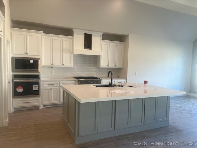 kitchen featuring wall chimney range hood, white cabinets, a kitchen island with sink, and sink