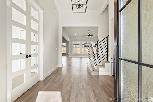 foyer entrance featuring ceiling fan with notable chandelier, wood finished floors, baseboards, french doors, and stairway