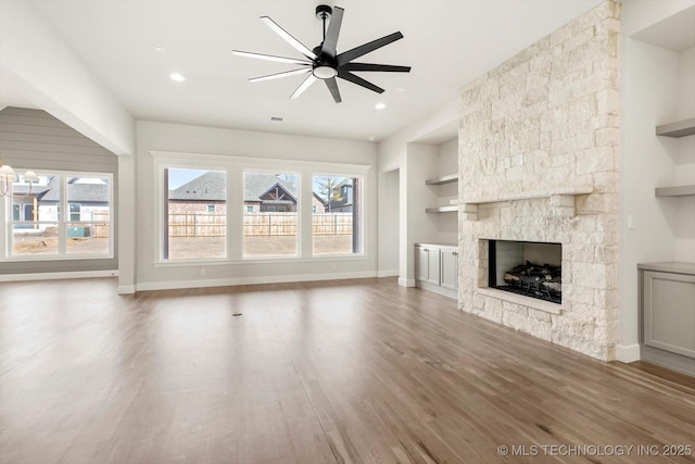 unfurnished living room with a fireplace, built in features, a wealth of natural light, and wood finished floors