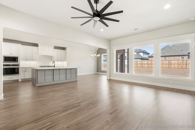 unfurnished living room with recessed lighting, ceiling fan with notable chandelier, a sink, wood finished floors, and baseboards