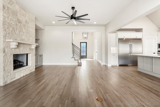 unfurnished living room featuring recessed lighting, a fireplace, wood finished floors, baseboards, and stairs