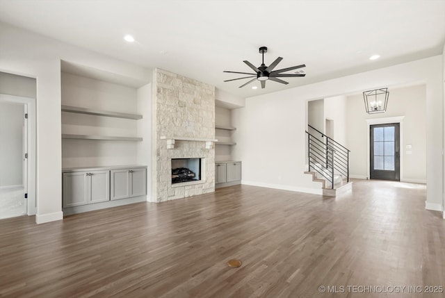 unfurnished living room featuring dark wood-type flooring, a fireplace, baseboards, built in features, and stairway