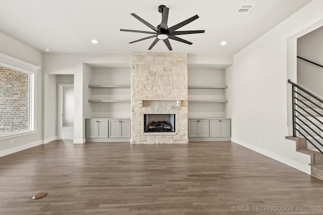 unfurnished living room with baseboards, visible vents, wood finished floors, stairs, and a fireplace