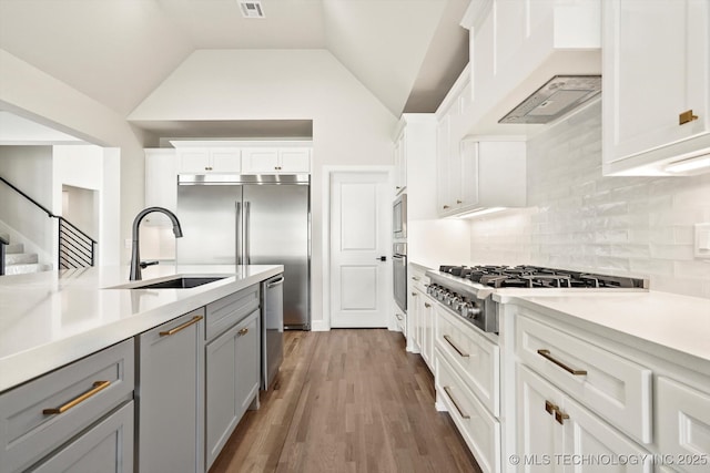 kitchen featuring built in appliances, light countertops, gray cabinets, and a sink