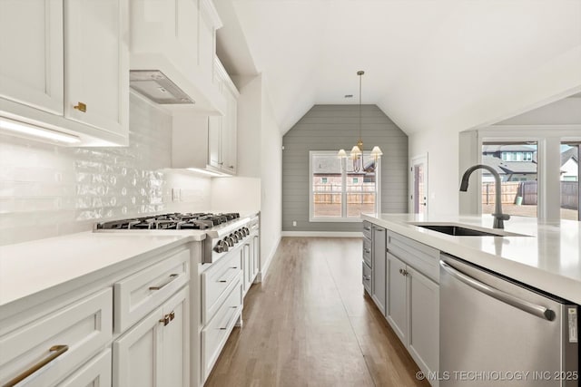 kitchen with a sink, vaulted ceiling, light countertops, appliances with stainless steel finishes, and backsplash