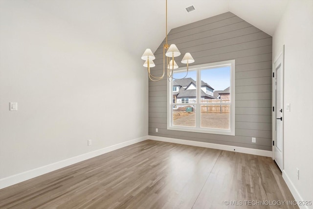 unfurnished dining area featuring lofted ceiling, an inviting chandelier, baseboards, and wood finished floors